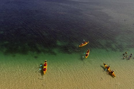 Kayakers setting off from beach into Coral Bay at Ningaloo Reef marine park, Western Australia.
